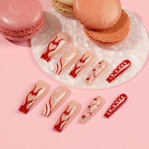 Long coffin press-on nails with red flame, heart designs and rhinestones on marble tray