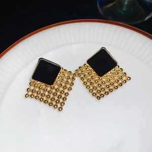 Close-up of diamond-shaped woven earrings in black enamel and gold finish on ceramic plate