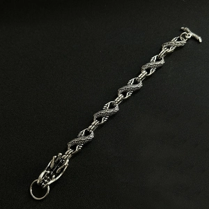 Detailed view of silver dragon scale chain bracelet with toggle clasp on black texture