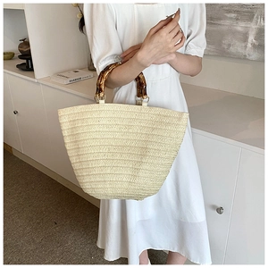 Detail of hand-woven straw tote with vintage bamboo handle on cream-colored dress