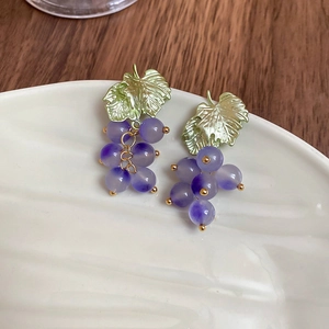 Detail of grape-shaped purple bead earrings with gold leaf accents on a ceramic plate