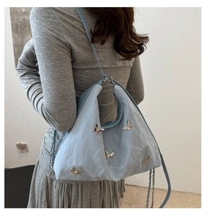 Detailed close-up of light blue shoulder bag featuring gold butterfly buckle and pleated texture