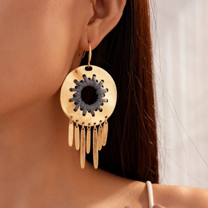 Détail de boucles d'oreilles bohèmes dorées avec corde tressée grise et franges en métal