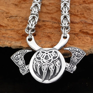 Detailed shot of Viking silver necklace with bear paw pendant and axes on wooden block