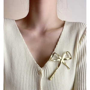Elegant gold metal bow brooch pinned on a beige knit cardigan for a stylish woman's look