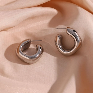 Macro shot of thick silver hollow hoop earrings on beige silk fabric background