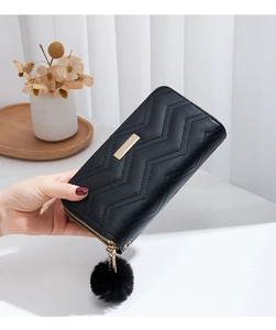 Detail of black wave quilted wallet featuring gold metal trim and fuzzy pompom tassel charm