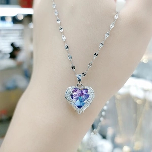 Detailansicht der silbernen Herz-Halskette mit blau-violetten Flügeln in der Hand