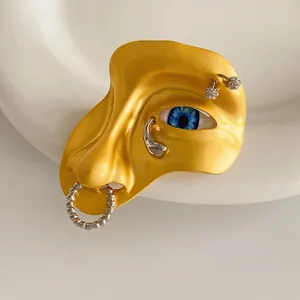 Artistic face brooch with blue eye and silver piercings on white ceramic plate