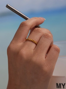 Detail of 18K gold plated gear shape ring worn by model with a beach background view