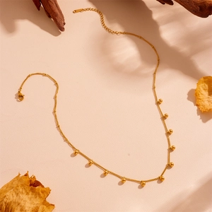 Close-up of a minimalist gold chain necklace with small metal beads on textured paper