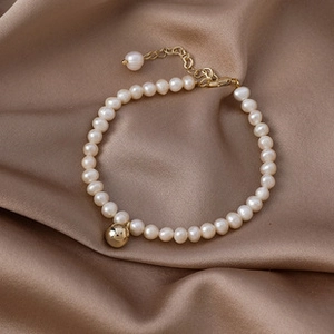 Detailed close-up of Baroque pearl bracelet with 14K gold plated bead on silk background