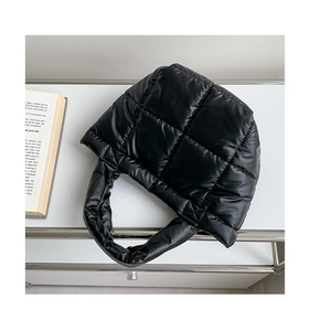 Detail of black quilted puffer bag with glossy rhombus stitching on white metal shelf