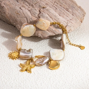 Detail of 18k gold chain bracelet with sea shell pendants on a beach sand background