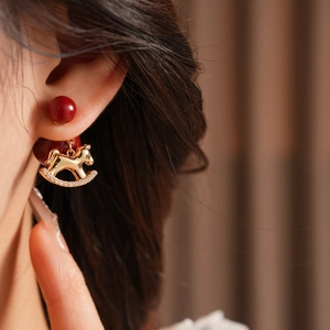 Model wearing gold rocking horse earrings with red beads and sparkling zircon stones
