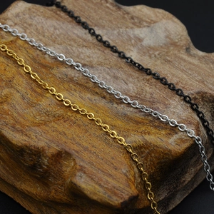 Detail of O-link chain necklaces in gold, silver, and black on dark wood background