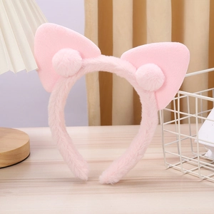 Detailed view of pink plush cat ear headband with soft pom-poms on a wooden table