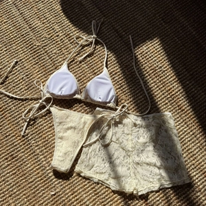 Detailed flat lay of cream lace three-piece bikini set with sheer boy shorts on textured rug