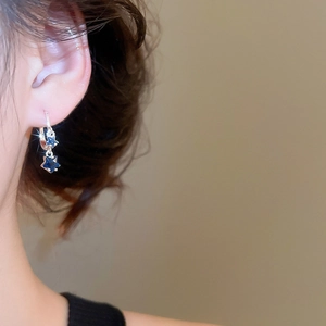 Close-up of a silver huggie earring featuring a delicate dark blue zircon star charm