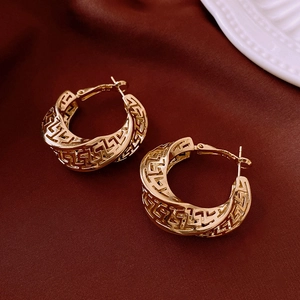 Macro view of gold hoop earrings with geometric Greek Key cut-out on red satin fabric
