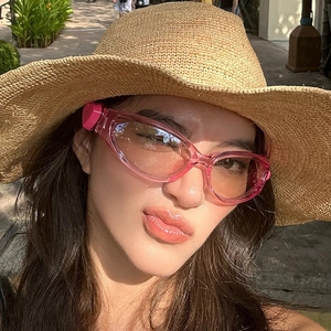 Close-up of pink jelly heart sunglasses with gradient lenses worn with a straw hat