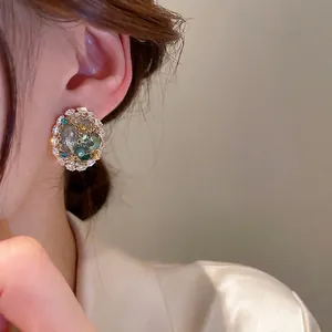 Elegant woven cluster stud earrings with green crystals and gold trim on model