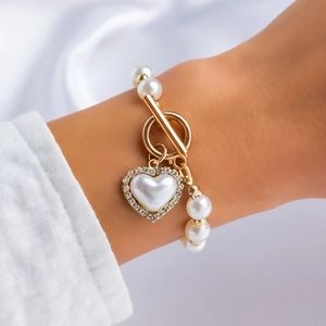 Close-up of pearl bracelet featuring a heart pendant and golden OT clasp on white silk