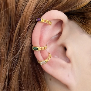 Detail view of gold cuff earrings featuring colorful crystals and chain link design