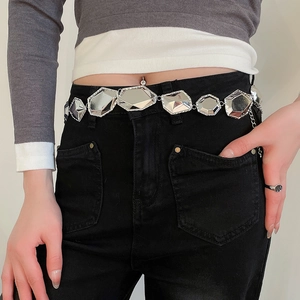 Gros plan d'une ceinture chaîne argentée à facettes géométriques sur un jean noir