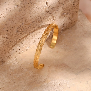 Detail of golden adjustable open bangle with vintage braided texture on stone surface