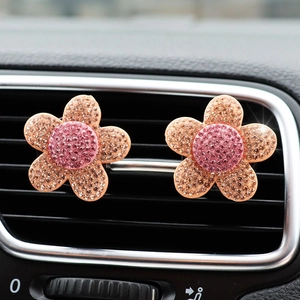 Close-up of sparkling pink and orange rhinestone flower car vent clips on a dashboard