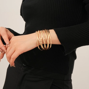 Detail of a multilayer gold layered cuff bracelet on a model wearing black knitwear