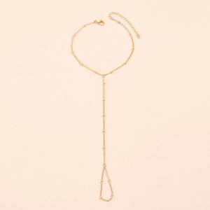 Detail of gold chain anklet with round beads and integrated toe ring on beige background