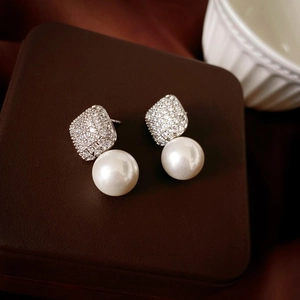 Detail of square zircon studs and elegant white pearl drop earrings on leather