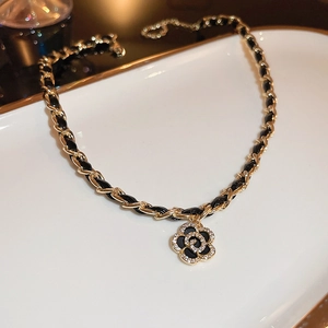 Detailed close-up of camellia pendant necklace with woven gold chain and black leather