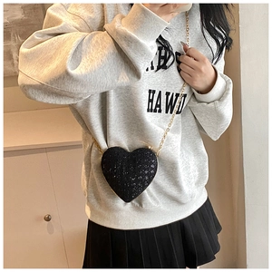Close-up of a black heart-shaped sequin crossbody bag with a gold chain strap on model