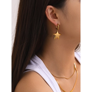 Close-up of polished 18k gold-plated star dangle earrings on a model with matching necklace