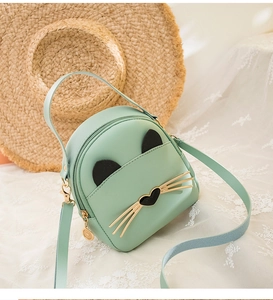 Detail of mint green cat-shaped crossbody bag on lace fabric with straw hat background