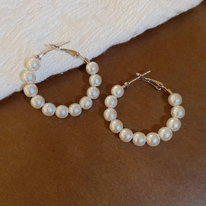 Close-up of geometric pearl hoop earrings with white beads on a textured surface