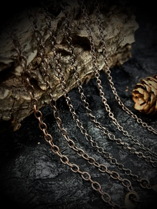 Macro shot of 60cm vintage bronze link chain draped over natural wood with pine cone accent