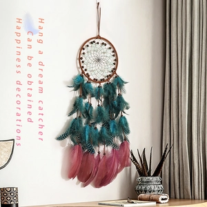 Vintage handmade dream catcher with teal and rose feathers hanging on a white wall