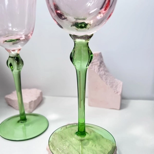 Close-up of pink crystal wine glass with decorative green stem on a minimalist surface