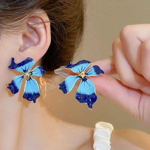 Détail de boucles d'oreilles fleur bleue avec pétales en émail et cœur doré