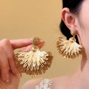 Detailed view of handmade raffia fan drop earrings with gold accents for beach vacations
