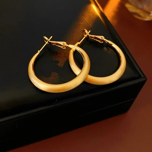 Close-up of golden matte C-shaped hoop earrings on a black jewelry box with soft lighting