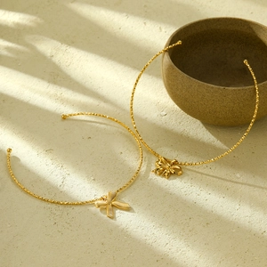 Elegant gold bow and flower pendant stainless steel necklaces on a textured surface