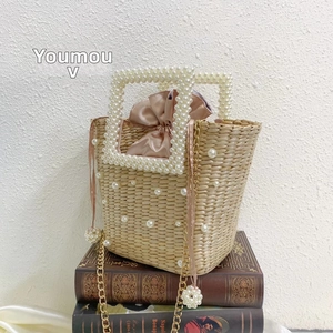 Detail of handmade straw bucket bag featuring pearl embellishments and a pink satin inner liner