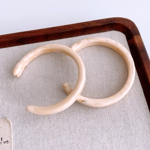 Close-up of marble pattern resin C-shape hoop earrings on a textured fabric