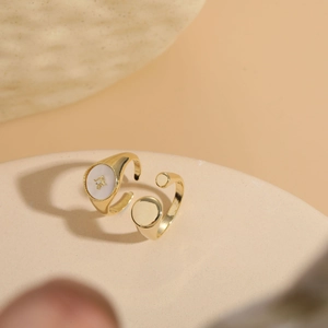 Detailed close-up of gold shell star signet ring and adjustable disc ring on a stone base