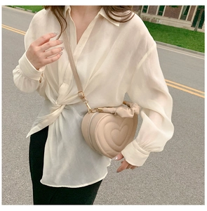 Close-up of beige heart-shaped crossbody bag with ruffled handle worn by a model